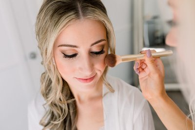 Bride gets blush applied to her cheek while getting ready for her wedding ceremony