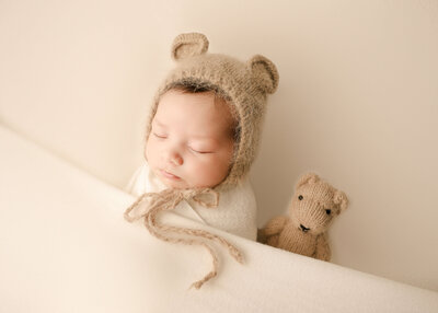 Baby posed with Teddy Bear bonnet sleeping in studio by Ashley Nicole in Temecula.