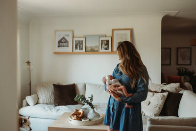 mom standing in living room with her new baby for their newborn photo session at home. 