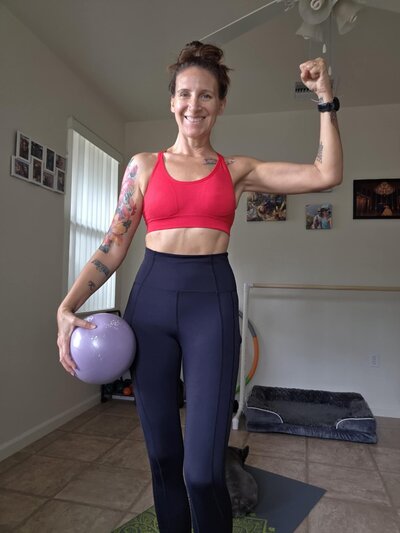 Picture of women with hair up in workout clothes with a pilates ball and a strong arm