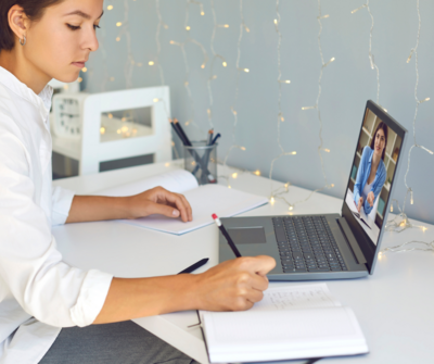 photo of a woman's arms typing on a laptop on a desk next to a cup of tea. 