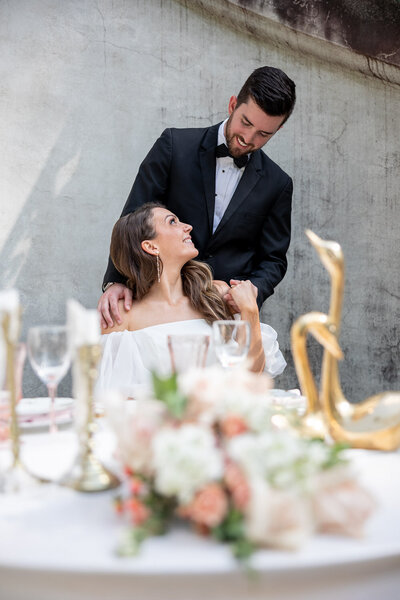 Photo by GreenPoint Photography - Bride and Groom looking into each others eyes with joy. The Bride is sitting behind a decorative table scape where her bouquet rests
