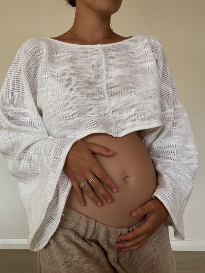 pregnant woman in white crop top cradling her bare belly