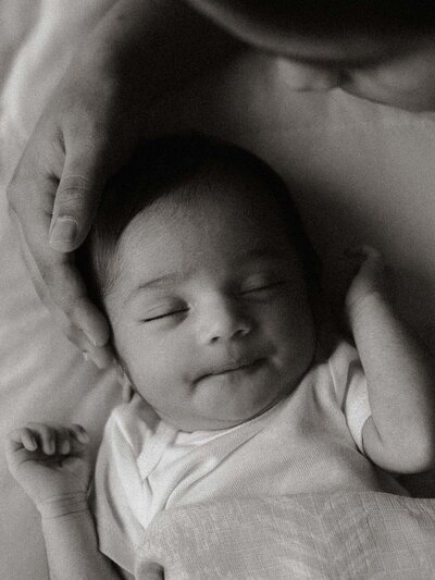 Close-up of a parent gently holding a newborn’s tiny hand, in black and white.
