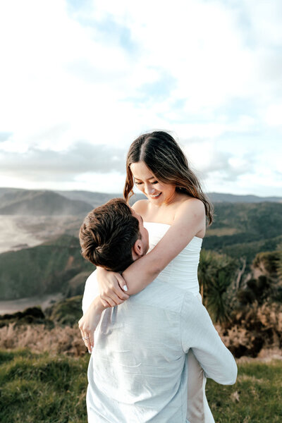 Bride-to-be embracing fiancé on hilltop overlooking ocean during New Zealand engagement shoot, photographed by Zanthe Vorsatz.