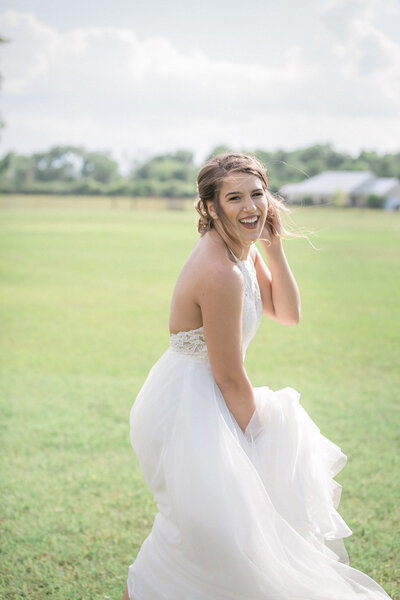the bride looks back at the camera, laughing, with her wedding venue in the distance