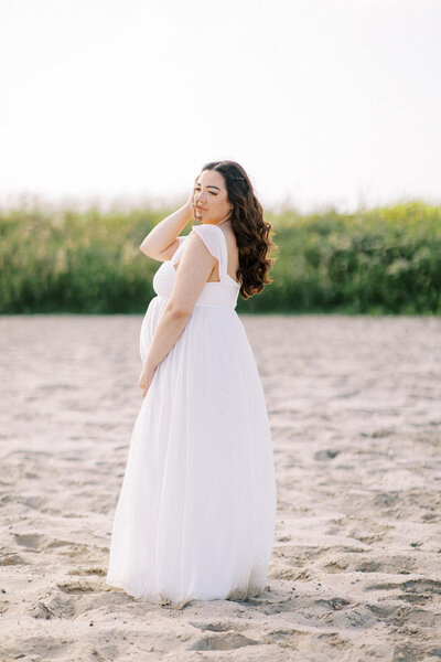 Een intiem moment van een zwangere vrouw, wandelend langs de waterkant, vastgelegd in een serene zwart-wit compositie.