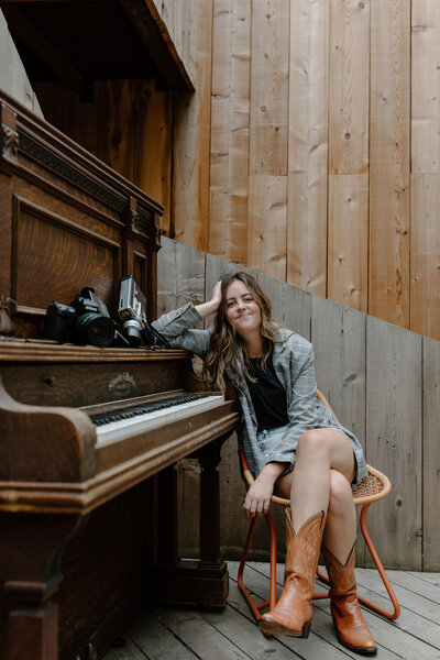 amanda pool leaning on piano with film cameras smiling at camera
