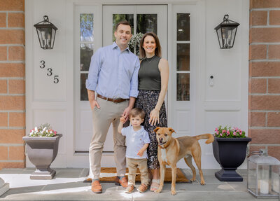 Family of three with their dog smiling on their front porch during a lifestyle family session.