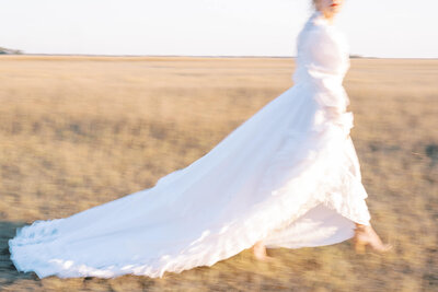 woman wearing a vintage gown walking across the marsh at sunset creating motion blur