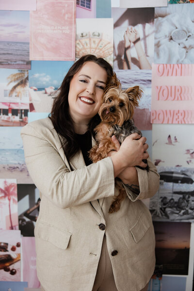 This is Mariah holding her dog Charlie against a background of a lot of pink imagery. She is smiling and hugging Charlie. 