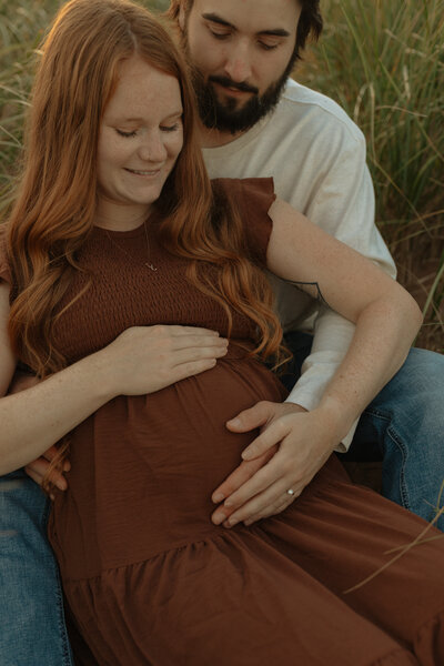 couple embrace and hold baby bump during maternity lifestyle session in pei