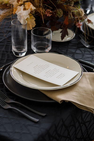 Chic wedding reception tables set with black and cream dishware, matte black flatware, and modern, wave-textured glassware