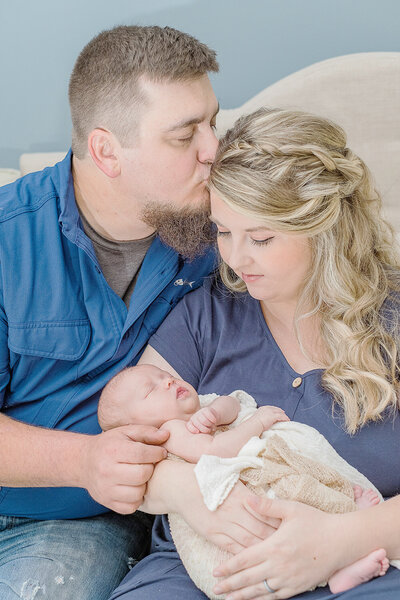 dad kissing mom's forehead as she looks down at newborn