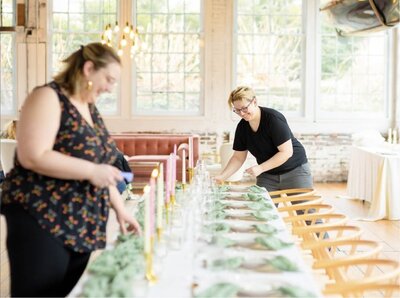 Rachel and Amy smiling while designing a wedding tablescape filled with pink and white candles