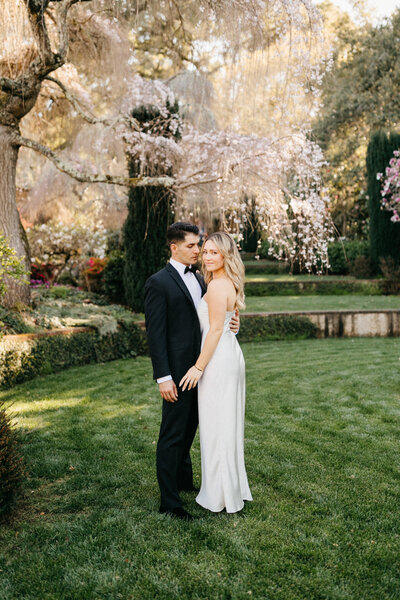 couple stands under cherry blossom tree at filoli estate