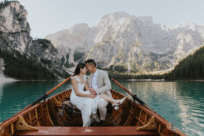 an engaged couple sit on a boat at Lago di Braies in the Dolomites with their foreheads touching with mountains behind them