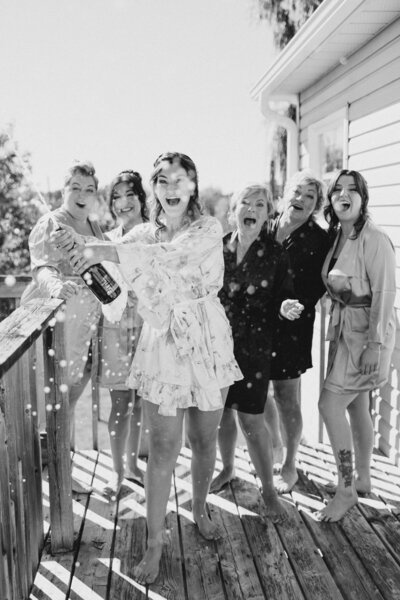 Bride popping champagne while getting ready with her bridesmaids, wearing satin robes