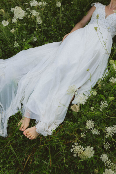 bride lays in dewey grass with the bottom of her dress wet and grassy