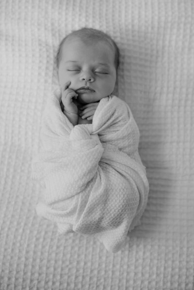 Black and white newborn photo of baby girl wrapped in blanket laying on bed in studio in Annapolis Maryland.