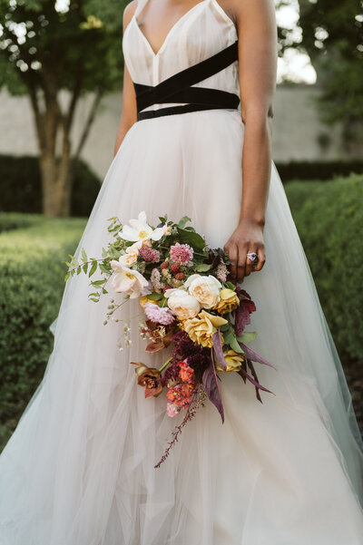 Bride wearing Carol Hannah gown holding blush gold coral burgundy and ivory bouquet in the War Memorial garden in Grosse Pointe