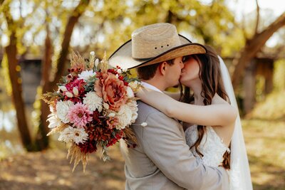 outdoor bridal photos with husband and wife kissing with bouquet