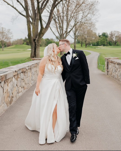 Bride and groom kissing as they walk over a stone bridge.