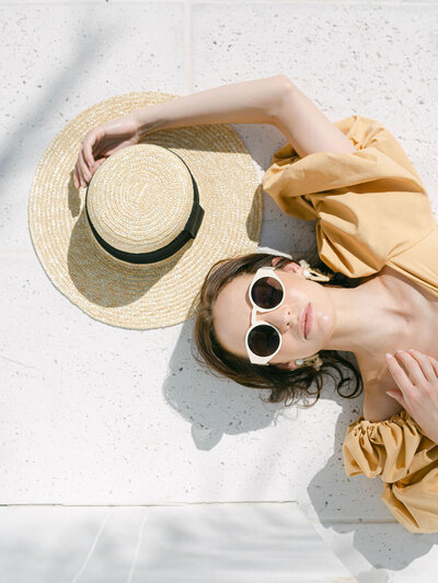 woman laying down with hat and wearing white Tol sunglasses