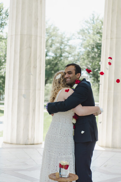 A newlywed couple hugging as rose petals are thrown around them 