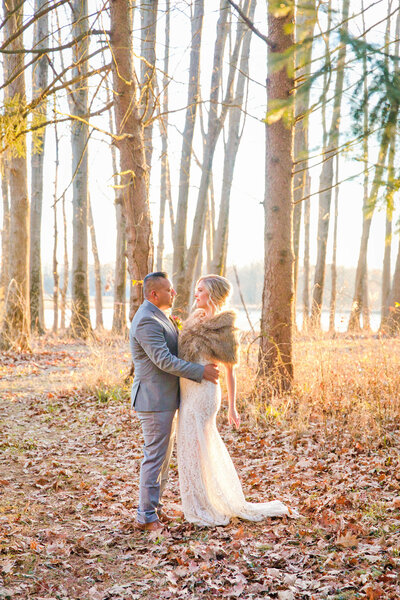groom in a grey suit holds onto bride in the middle of the forest as the sunsets