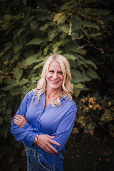 Melanie Kasten in blue top, smiling, in front of trees