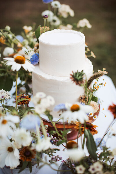 Two-tier wedding cake decorated with wildflowers at an outdoor Maine wedding reception.