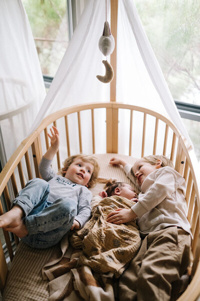 newborn baby in cot with big brothers
