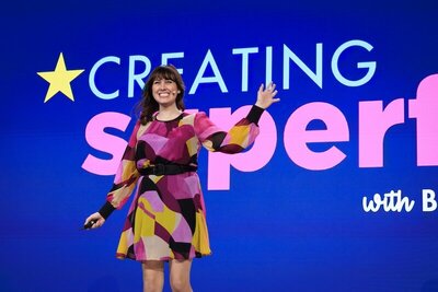 Brittany Hodak delivering a keynote on stage, waving to the audience