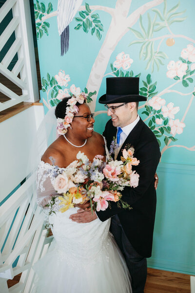 A wedding couple holding a bouquet of flowers standing in front of a painted wall