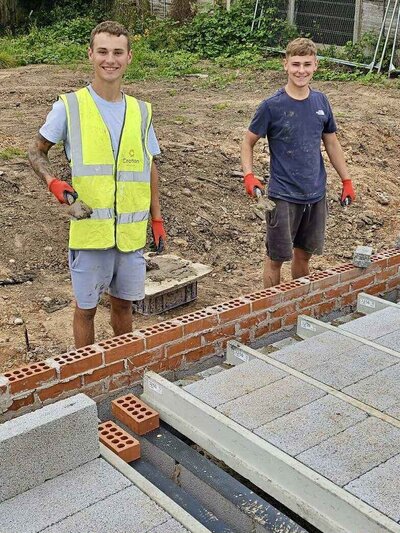 Two young bricklayers Alfie & Ed smiling at a construction site.