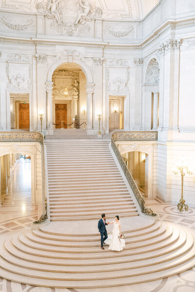 bright and airy image of a bride and groom at the bottom of the grand staircase in the San Francisco City Hall