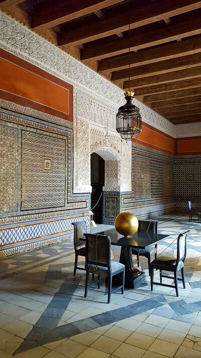 Ornate Moorish-style room with intricate tilework, carved archways, and a wooden coffered ceiling at Casa de Pilatos in Seville, Spain ©Stephanie Dosch | theViatrix Luxury Travel