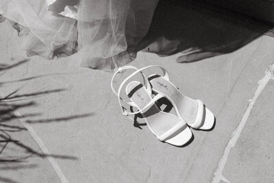 Bride's white strappy wedding shoes sitting on the floor