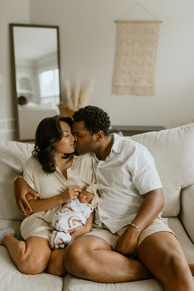 couple kisses on couch with newborn baby