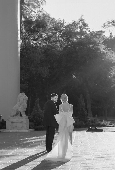 Black and white photo of bride and groom walking hand in hand at Chateau Nouvelle in Houston, Texas with dramatic backlighting and elegant architecture