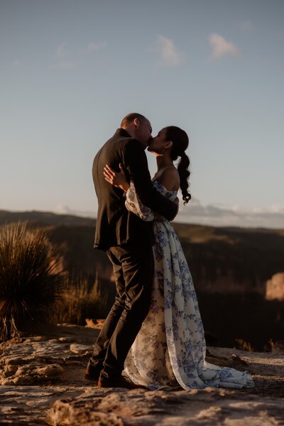 A couple kissing with mountain views in the background at golden hour while they embrace