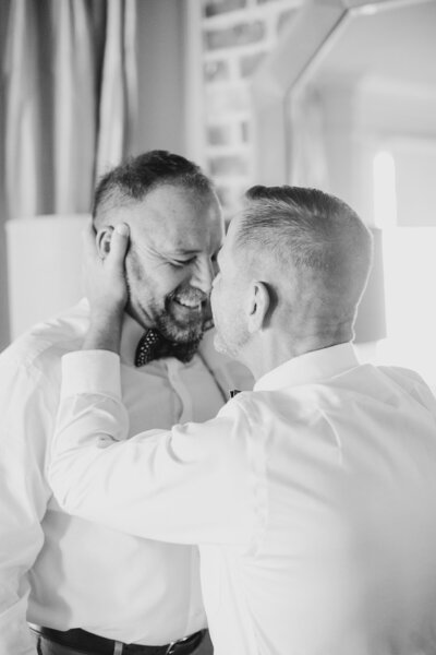 Groom holding groom's head while smiling.
