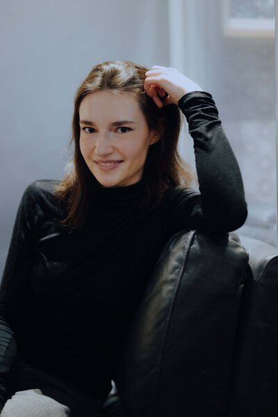 Woman with dark hair wearing black turtleneck resting smiling at camera