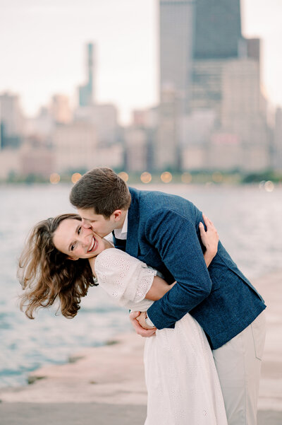 man kissing his finance on the cheek with a river and the Chicago cityscape in the background