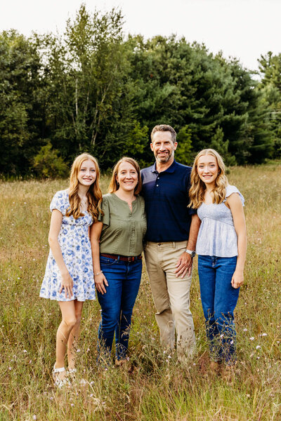 mother and father standing with their two teenage daughters in a field with wildflowers for their family photo session