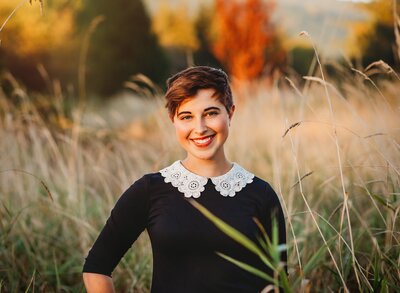 Young woman smiles in a field of tall grass for senior portrait