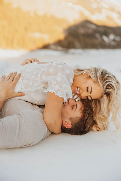 A couple laughing together as the woman lays on top of the man during a joyful wedding photo session.