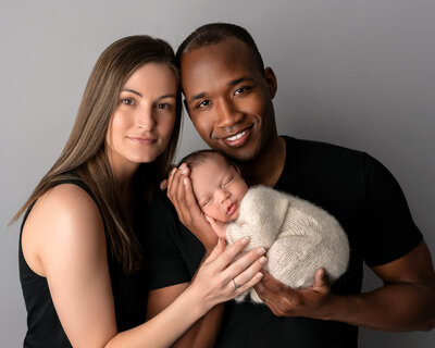 Studio newborn photo of parents holding swaddled baby boy in cream wrap, taken by Hello Photography in Austin, Texas.