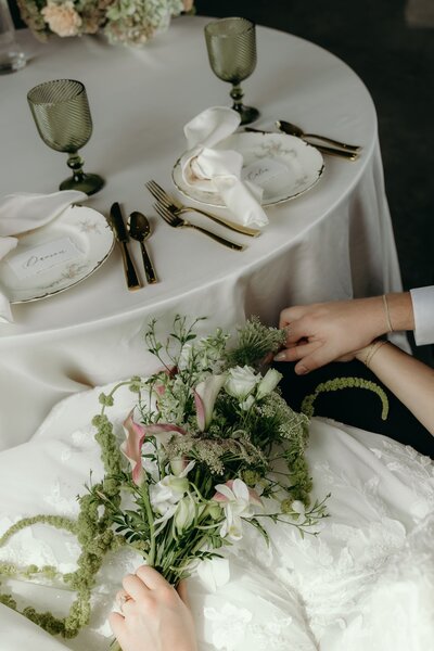 A bride and groom tenderly hold hands seated behind their sweetheart table.